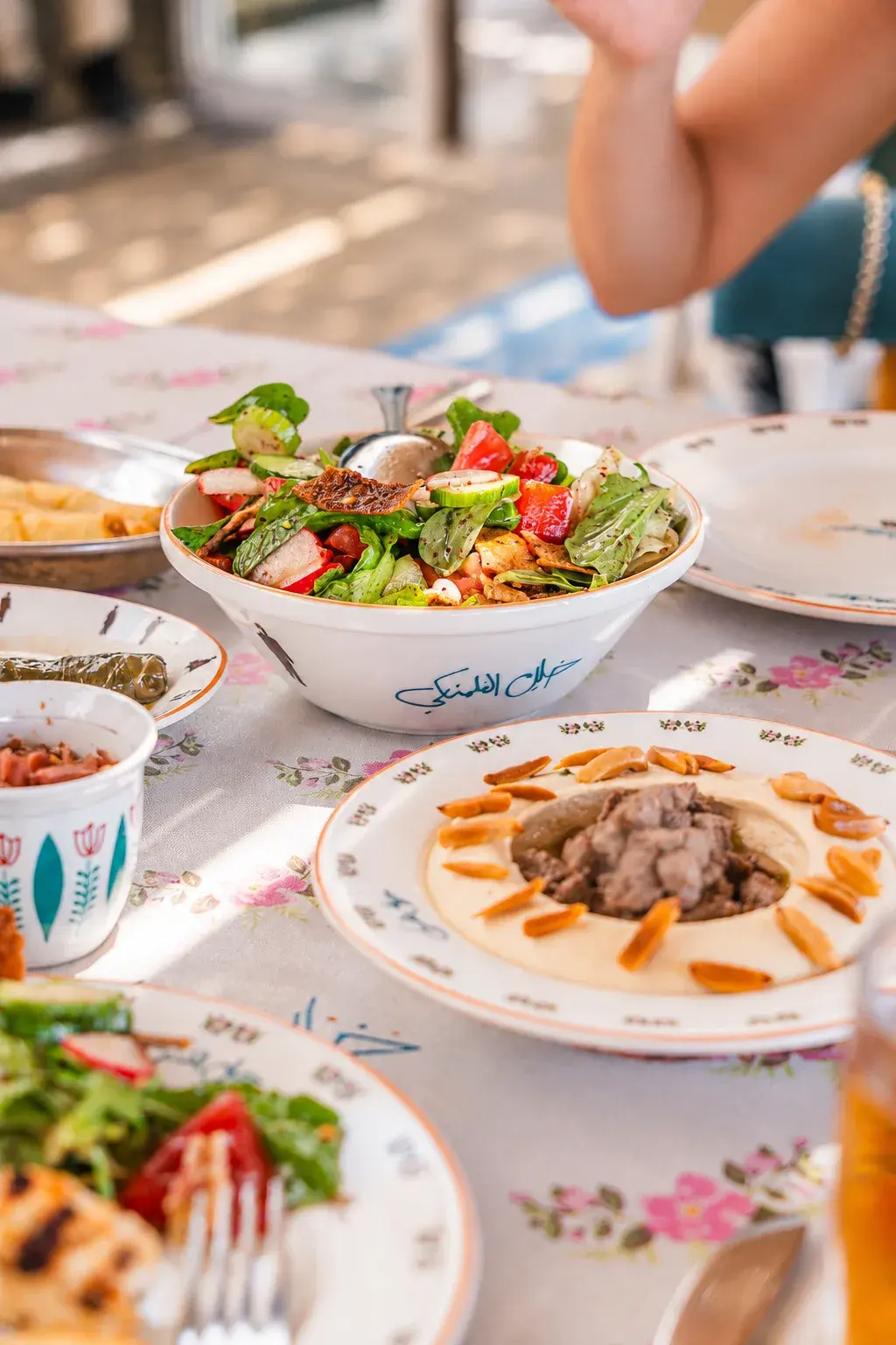 Fattoush and hummus topped with meat and pine nuts on the floral tablecloth